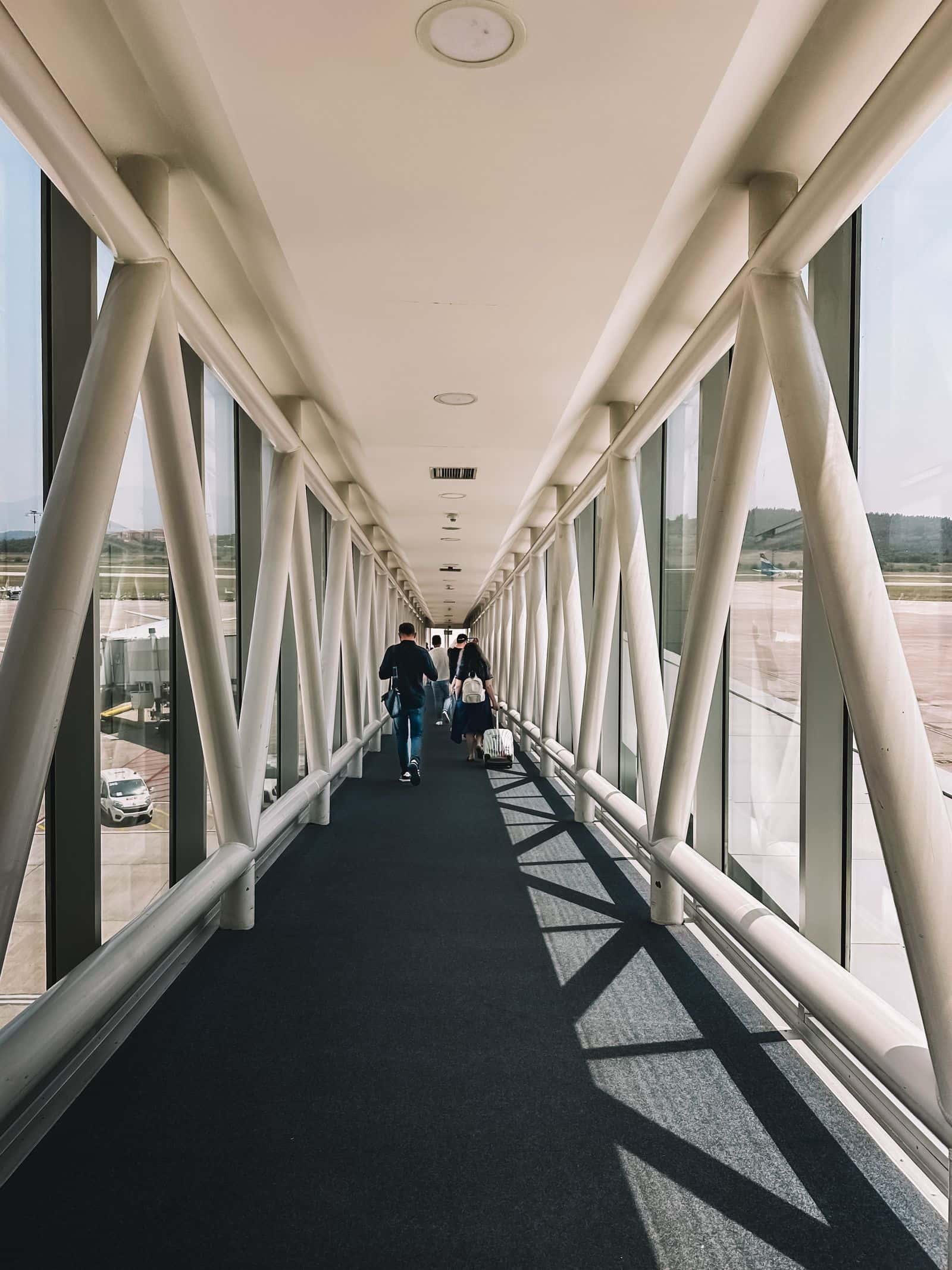 Travelers walking down a sunlit airport jet bridge toward their gate