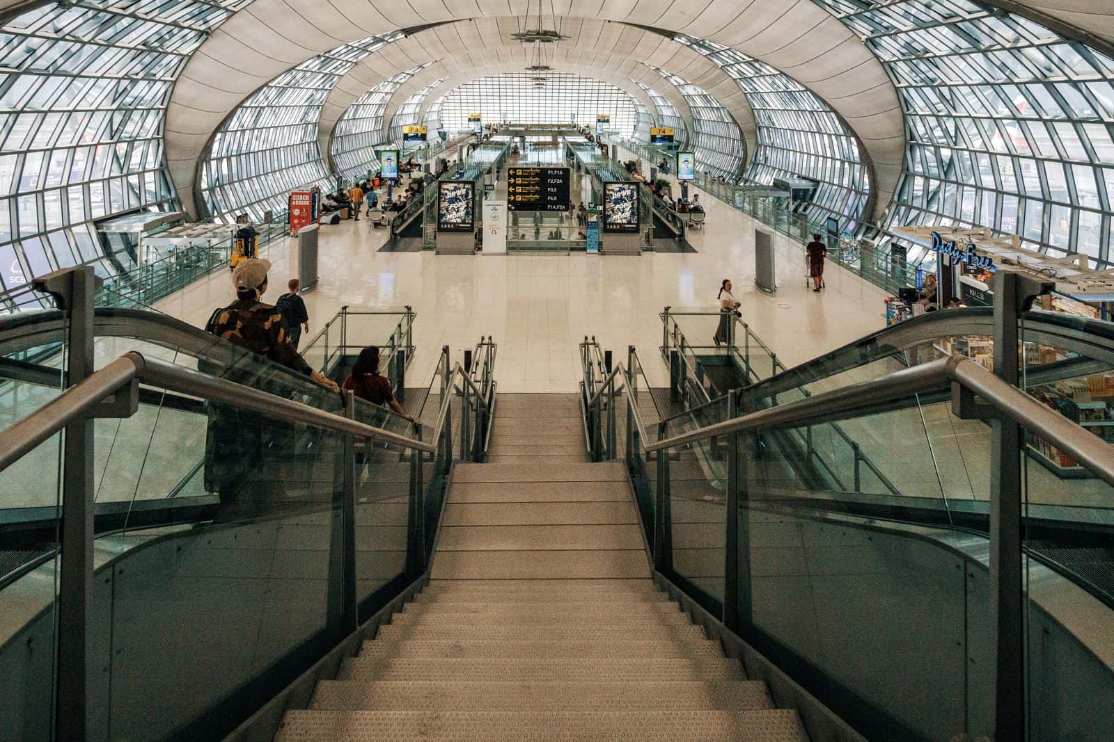 Sweeping staircase beneath a curved glass terminal roof at a modern international airport