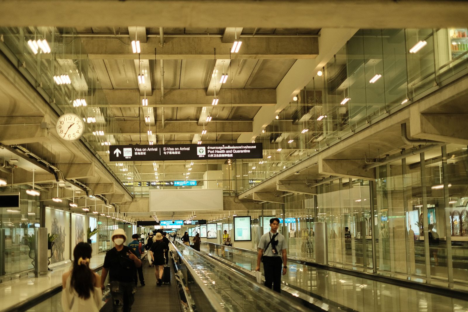 Travellers walking along a moving walkway in a bright modern airport terminal